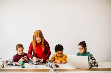Robot sınıfında elektrikli oyuncak ve robot programlayan bir grup mutlu çocuk.