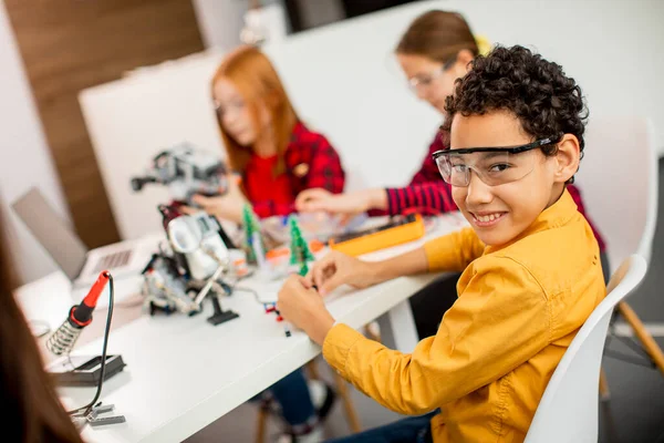 Group of happy kids programming electric toys and robots at robotics classroom