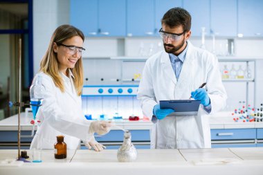 Genç araştırmacılar bir kimya laboratuvarının masasında dumanla deney yapıyorlar.