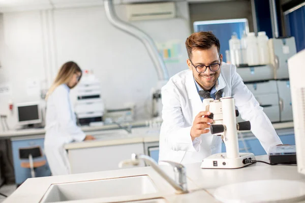 Handsome young scientist in white lab coat working with binocular microscope in the material science lab