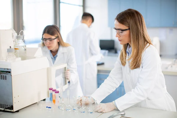 Young female scientists in a white lab coat putting vial with a sample for an analysis on a ionchromatography system in biomedical lab