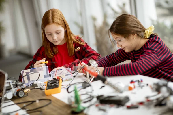 Group of cute little girls programming electric toys and robots at robotics classroom