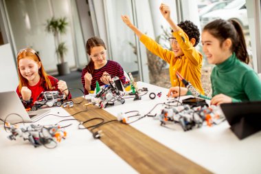 Robot sınıfında elektrikli oyuncak ve robot programlayan bir grup mutlu çocuk.