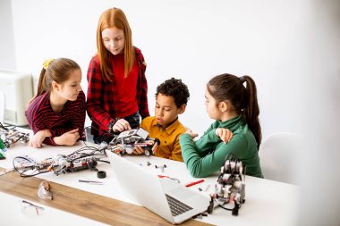 Robot sınıfında elektrikli oyuncak ve robot programlayan bir grup mutlu çocuk.