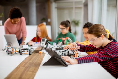 Bir grup mutlu çocuk ve dizüstü bilgisayarı olan Afrika kökenli Amerikalı kadın fen öğretmenleri robot sınıfında elektrikli oyuncaklar ve robotlar programlıyorlar.