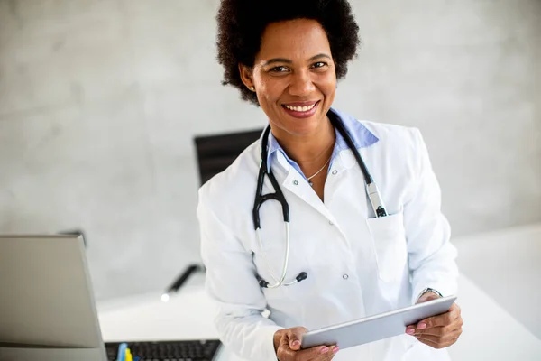 Afroamerykańska Lekarka Białym Płaszczu Stetoskopem Stojąca Przy Biurku Trzymająca Cyfrową — Zdjęcie stockowe