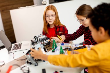 Robot sınıfında elektrikli oyuncak ve robot programlayan bir grup mutlu çocuk.