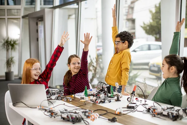 Group of happy kids programming electric toys and robots at robotics classroom