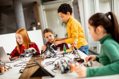 Robot sınıfında elektrikli oyuncak ve robot programlayan bir grup mutlu çocuk.