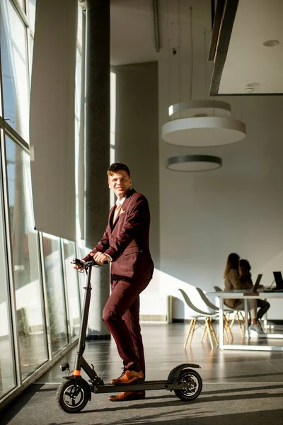 Przystojny Młody Biznesmen Stojący Przy Oknie Biurowym Skuterem Elektrycznym — Zdjęcie stockowe
