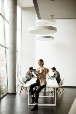 Modern bir ofiste, ekibinin önünde dijital tablet kullanan genç bir iş kadını.