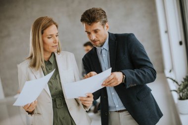 Ofiste genç insanlarla el ele kağıt tartışan bir adam ve kadın arkalarında çalışıyor.