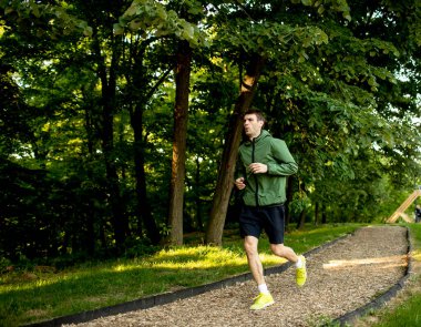 Güneşli yeşil parkta spor yaparken koşan yakışıklı genç adam.