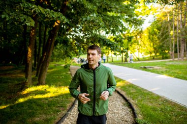 Güneşli yeşil parkta spor yaparken koşan yakışıklı genç adam.