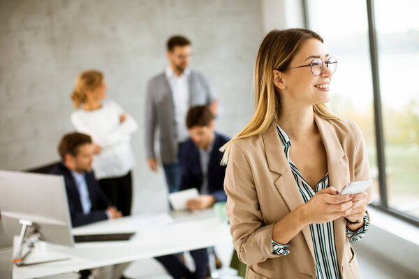 Красивая молодая деловая женщина, стоящая в офисе и судясь с мобильным телефоном перед своей командой