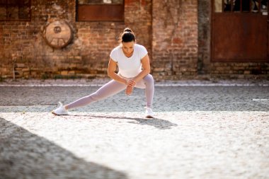 Şehir ortamında eğitim sırasında esneme hareketleri yapan güzel bir genç kadın.