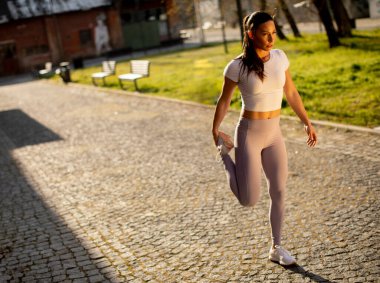 Şehir ortamında eğitim sırasında esneme hareketleri yapan güzel bir genç kadın.