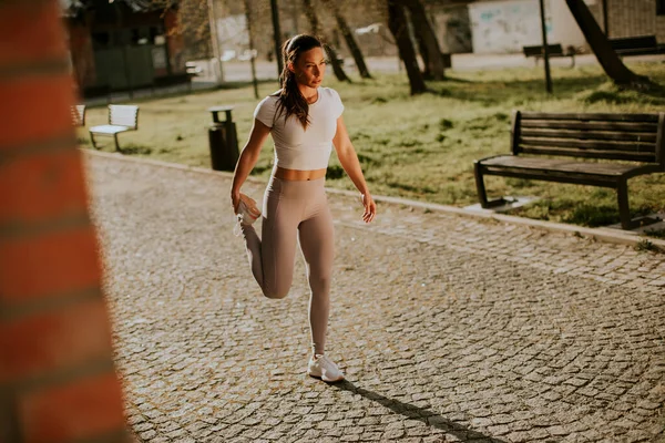 Şehir ortamında eğitim sırasında esneme hareketleri yapan güzel bir genç kadın.