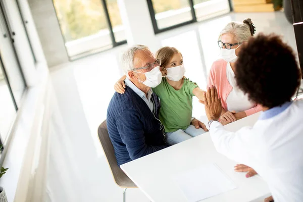 Senior couple with cute granddaughter black female doctor in the office