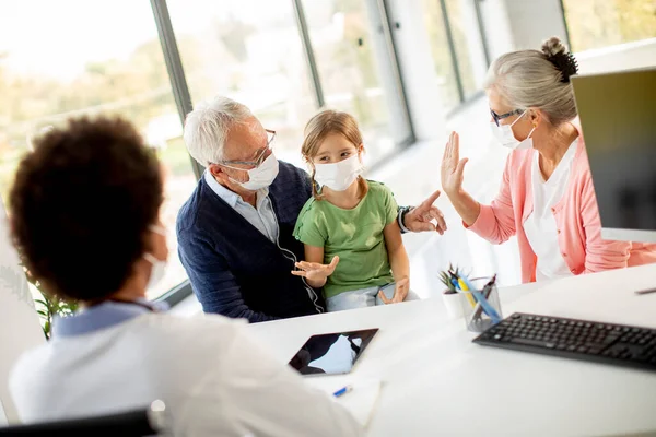 Senior couple with cute granddaughter black female doctor in the office