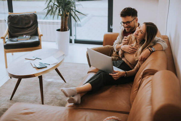 Handsome young couple using laptop together while sitting on sofa at home