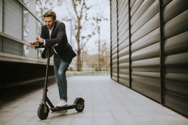Elektrikli scooter 'da cep telefonu kullanan yakışıklı genç işadamı.