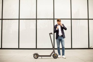 Elektrikli scooter 'da cep telefonu kullanan yakışıklı genç işadamı.