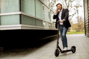 Elektrikli scooter 'da cep telefonu kullanan yakışıklı genç işadamı.