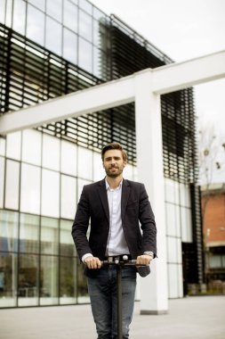 İş görüşmesindeki bir ofis binasının önünden elektrikli scooterla geçen sıradan giysili yakışıklı bir iş adamı.