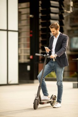 Elektrikli scooter 'da cep telefonu kullanan yakışıklı genç işadamı.