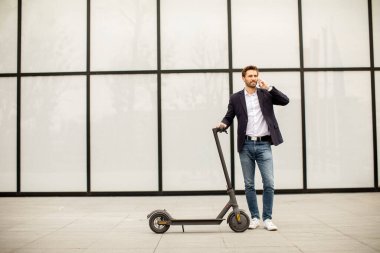 Elektrikli scooter 'da cep telefonu kullanan yakışıklı genç işadamı.