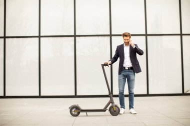 Elektrikli scooter 'da cep telefonu kullanan yakışıklı genç işadamı.