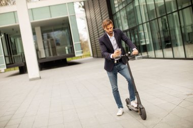 Elektrikli scooter 'da cep telefonu kullanan yakışıklı genç işadamı.