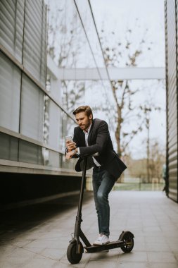 Elektrikli scooter 'da cep telefonu kullanan yakışıklı genç işadamı.