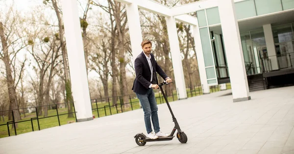 Handsome young business man in a casual clothes riding an electric scooter by an office building on a business meeting