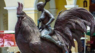 HAVANA, CUBA - 4 Temmuz 2017: Havana, Küba 'daki Plaza Vieja' da Roberto Fabelo 'nun Horoz Heykeli Üzerine Kız. Bu bronz heykel 2012 'de dikildi..