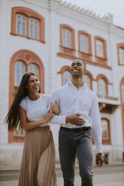 Sokakta yürüyen yakışıklı, etnik çeşitlilikte genç bir çift.