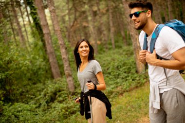 Gülümseyen genç bir çift yaz günü ormanda sırt çantalarıyla yürüyorlar.