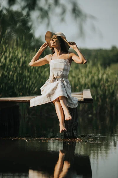 穏やかな湖の木の桟橋で若い女性をリラックスさせ — ストック写真