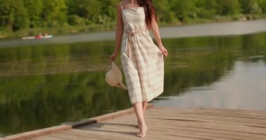 Sakin gölün kıyısındaki ahşap iskelede yürüyen rahatlatıcı genç kadın.