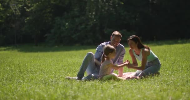 Ευτυχισμένη νεαρή οικογένεια με χαριτωμένη μικρή κόρη διασκεδάζουν στο πάρκο σε μια ηλιόλουστη μέρα — Αρχείο Βίντεο
