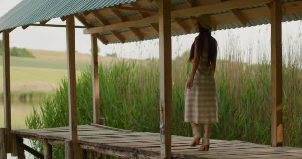 Расслабляющая молодая женщина, идущая по деревянному пирсу на спокойном озере — стоковое видео
