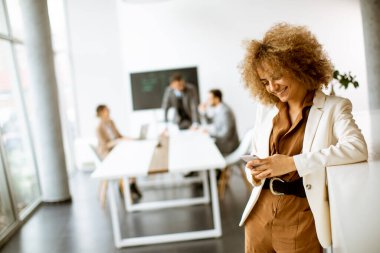 Modern ofiste cep telefonu kullanan gülümseyen genç iş kadını.