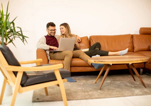 自宅でソファに座っている間に一緒にラップトップを使用してハンサムな若いカップル — ストック写真