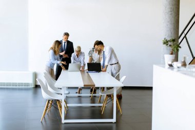 Genç yetişkinler ve kıdemli bayan meslektaşlarıyla birlikte bir grup iş adamı modern parlak ofis içlerinde toplanıyorlar.