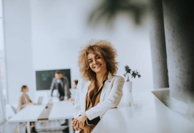 Gülümseyen genç iş kadını modern ofiste duruyor.