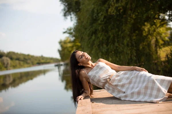 穏やかな湖の木の桟橋で若い女性をリラックスさせ — ストック写真