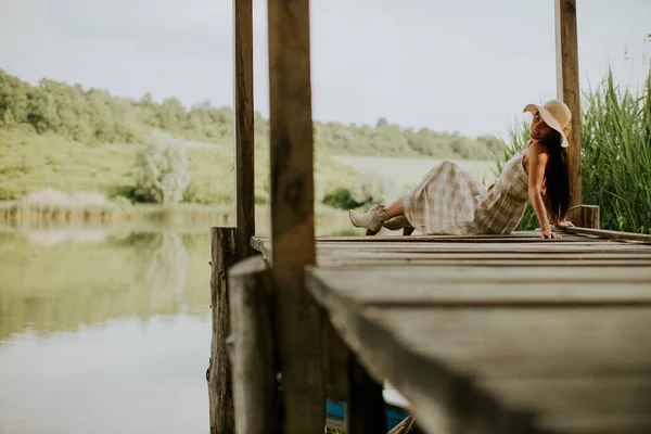 在平静的湖畔的木制码头上让年轻女子放松 — 图库照片