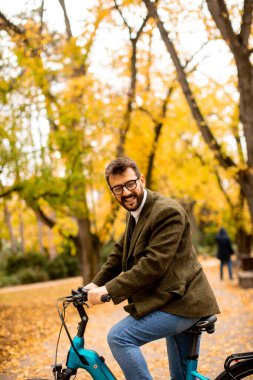 Sonbahar parkında elektrikli bisikletli yakışıklı bir genç.
