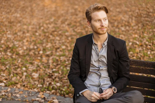 Young man at the bench in autumn park — Stock Photo, Image